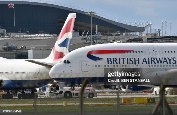 Union flag flies above a hangar as a British Airways operated Airbus A380 passenger jet is moved by an aircraft tractor at Heathrow Airport, west of...