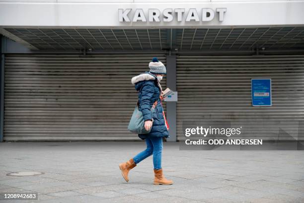 Woman wearing a face mask to limit the spread of the novel coronarivurs walks past a department store of German retail chain Karstadt of the Galeria...