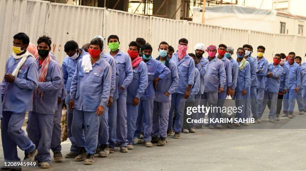 Foreign workers wearing scarves and masks to protect their faces, stand in line to board a bus transporting them to their workplace, during the novel...