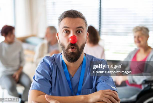 a portrait of doctor with red clown nose in hospital, patients in the background. - clown's nose stock pictures, royalty-free photos & images
