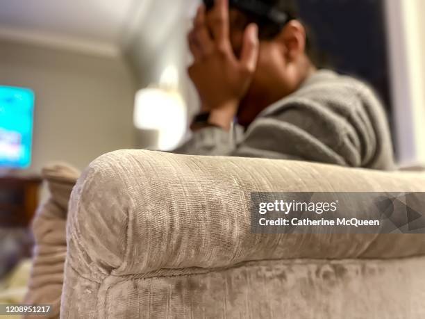 african-american woman holds head in hands on couch watching television - chronic fatigue stock-fotos und bilder