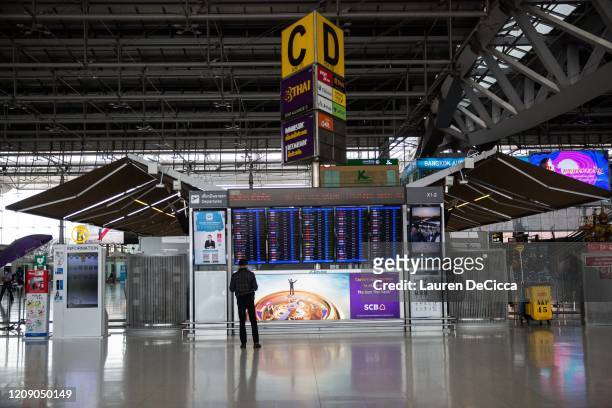 People check the departure announcement board at an empty Suvarnabhumi Airport departure hall after Thailand's government announced that the country...