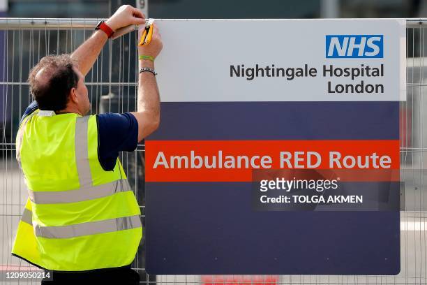 Worker affixes a new sign to a fence at the ExCeL London exhibition centre, which has been transformed into the "NHS Nightingale" field hospital, in...