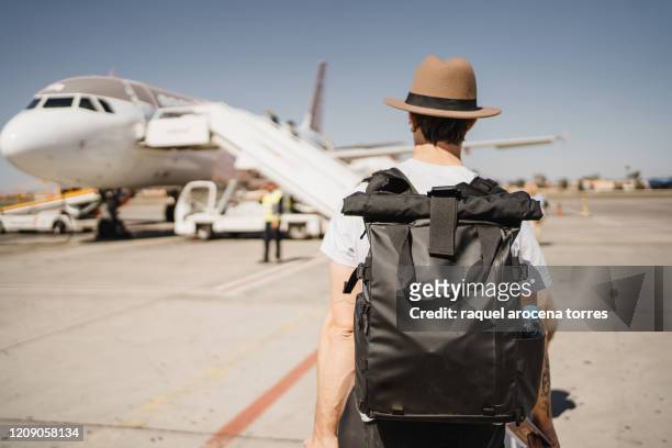 young white man with hat and suitcase walking through the airport on the runway towards his airplane - embarks stock pictures, royalty-free photos & images