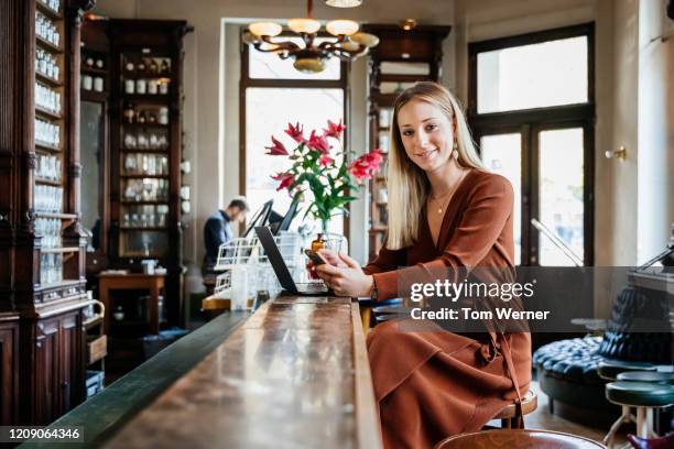 portrait of woman sitting at restaurant bar working on laptop - vestito marrone foto e immagini stock