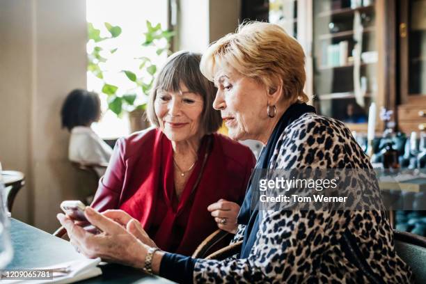 two mature ladies looking at smartphone in restaurant - bonding stock pictures, royalty-free photos & images