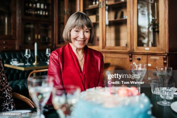 mature woman smiling while looking at birthday cake - 80 jahre torte stock-fotos und bilder