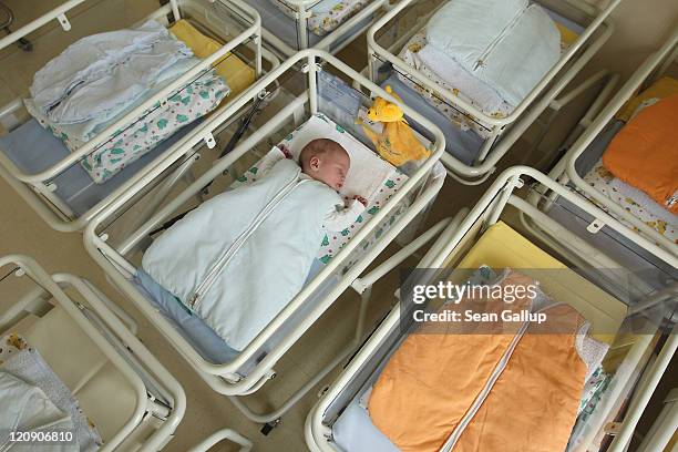 Day-old newborn baby, who has been placed among empty baby beds by the photographer, lies in a baby bed in the maternity ward of a hospital on August...