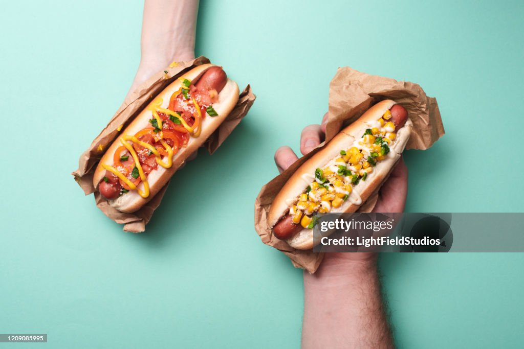 裁剪視圖的男人和女人拿著兩個美味的熱狗在藍色紙