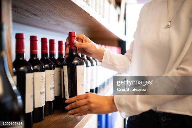 female hands arranging wine bottles on shelf at store - bottle shop stock pictures, royalty-free photos & images