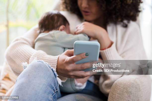 new mom uses smartphone while holding her baby boy - baby text stock pictures, royalty-free photos & images