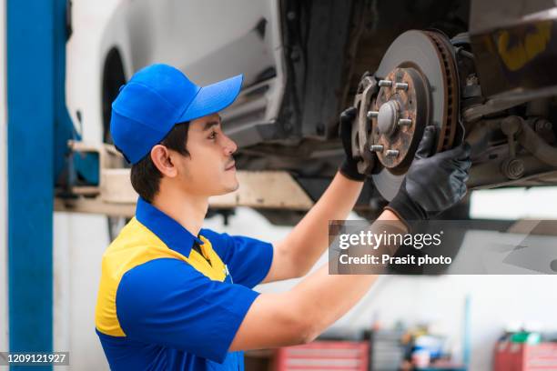 portrait of asian man car mechanic in blue uniform is checking and repairing disc break from vehicle while working in auto service. repair, car service and maintenance concept. - car brakes stock-fotos und bilder