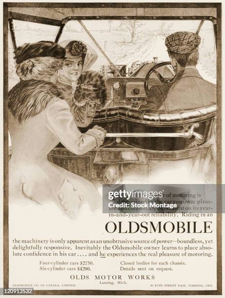 An Oldsmobile car interior is pictured in a magazine advertisement from 1909. The car, which is on a country road, has two women and a man seated...
