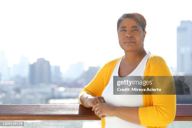 portrait of an african-american woman with a serious expression and short hair, wearing a yellow sweater, stands in an outdoor environment with an urban setting in the background. - woman short hair serious stock pictures, royalty-free photos & images