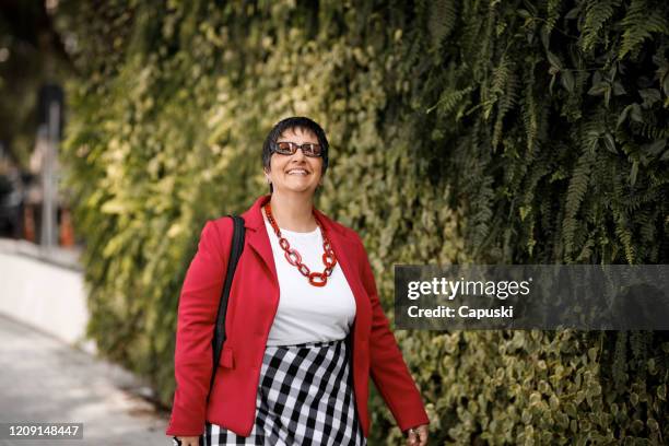 donna anziana che si gode una passeggiata di fronte a un giardino verticale - red coat foto e immagini stock