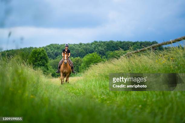 woman riding horse over pasture on thundery day - gallop animal gait stock pictures, royalty-free photos & images
