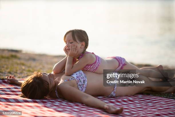woman sunbathing with daughter at lakefront - girls swimwear stock pictures, royalty-free photos & images