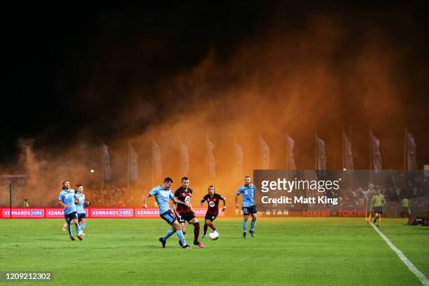 Ryan Mcgowan of Sydney FC is challenged by Mitchell Duke of the Wanderers as a flare is lit up in the crowd during the round 18 A-League match...