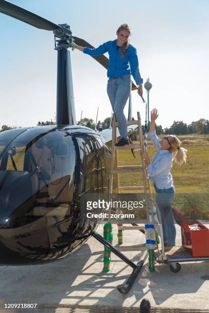 young woman on the ladder by the helicopter giving wrench to her colleague - vip pass stock pictures, royalty-free photos & images