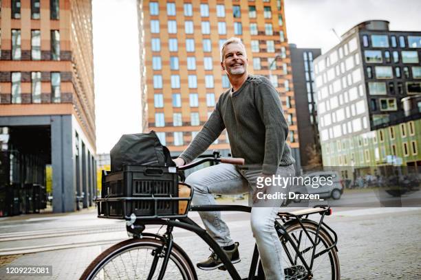 volwassen grijs haar zakenman die fiets berijdt en tot milieu-vriendschappelijke milieu bijdraagt - amsterdam bike stockfoto's en -beelden