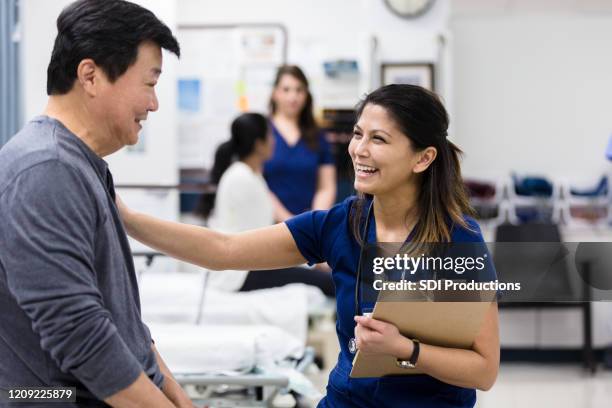 after finishing paperwork, nurse smiles and pats senior man - urgent care stock pictures, royalty-free photos & images