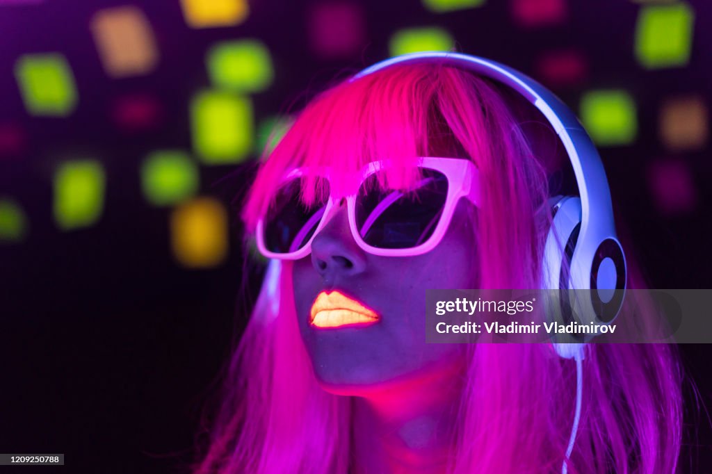 Woman with pink colored hair and sunglasses listening music