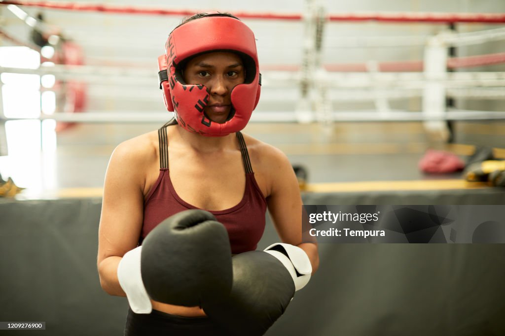 Young hispanic woman exercising in a boxing gym wearing a protective helmet.