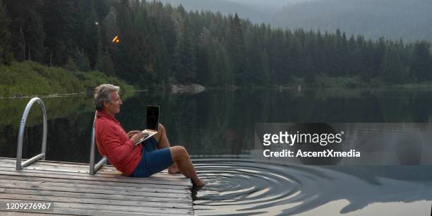 de rijpe mens pauzeert op houten pijler, kijkt uit over meer - rode korte broek stockfoto's en -beelden