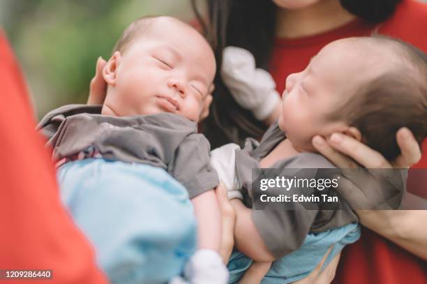 2 asian twin baby boy carried by their grandmother and mother - identical twin stock pictures, royalty-free photos & images