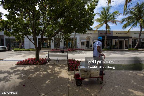 Post office worker carries mail bins past luxury stores closed on Worth Avenue in Palm Beach, Florida, U.S., on Friday, April 3. 2020. With more than...