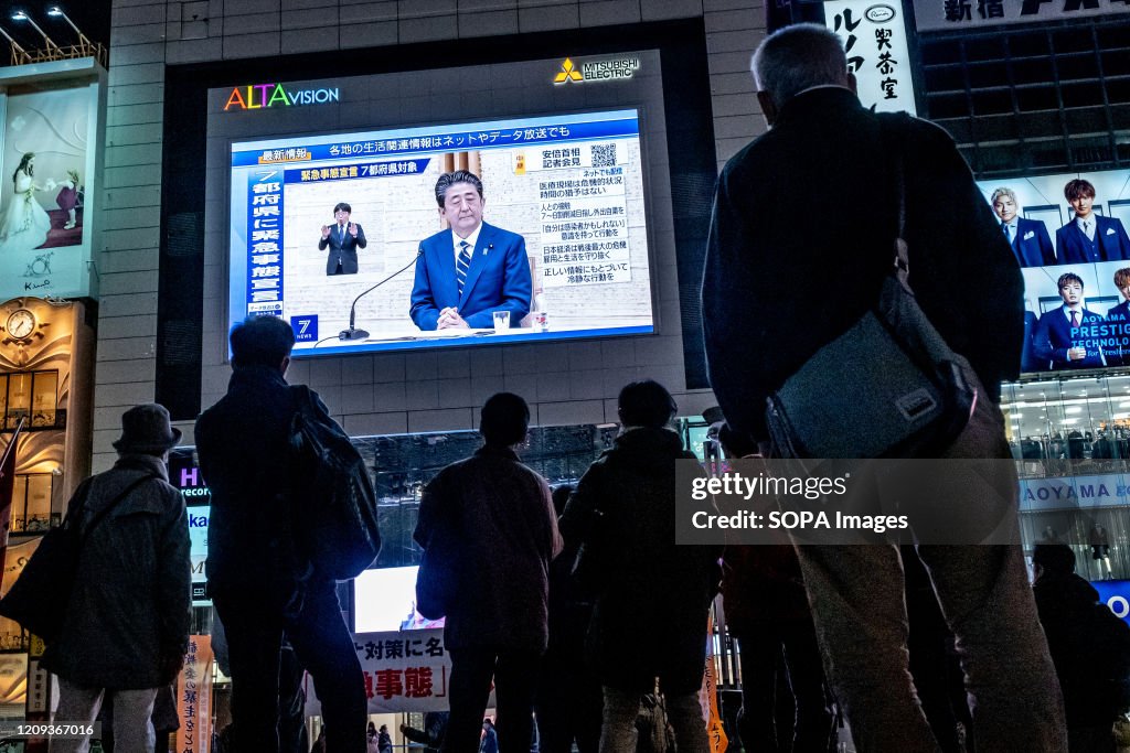 People seen standing in fron of a large television screen as...