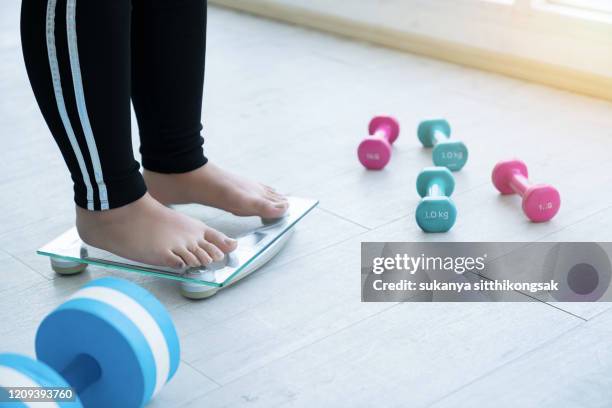 close up legs of overweight woman checking her weight scales and drumbell beside her. - fat woman stock-fotos und bilder
