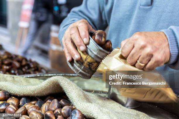 human hands fill a paper envelope with roasted chestnuts. - chestnut food stockfoto's en -beelden