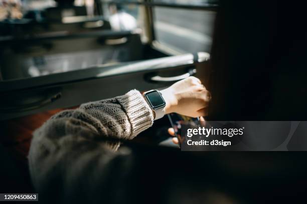 over the shoulder view of young asian woman holding smartphone and checking time on smartwatch while commuting in the city riding on a minibus - public transport stock pictures, royalty-free photos & images