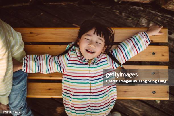 top down view of lovely little girl lying relaxingly on a bench in park - girl lying down stock pictures, royalty-free photos & images