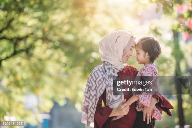 an asian modern muslim malay woman with hijab and sunglasses carrying her daughter outdoor on the street of kuaala lumpur bonding time - malay culture stock pictures, royalty-free photos & images