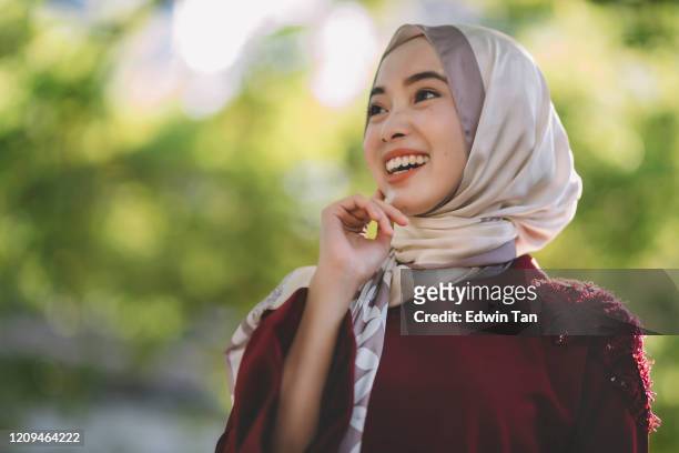 a modern muslim women portrait outdoor during day time in capital city of kuala lumpur with hijab and traditional clothing looking away smiling