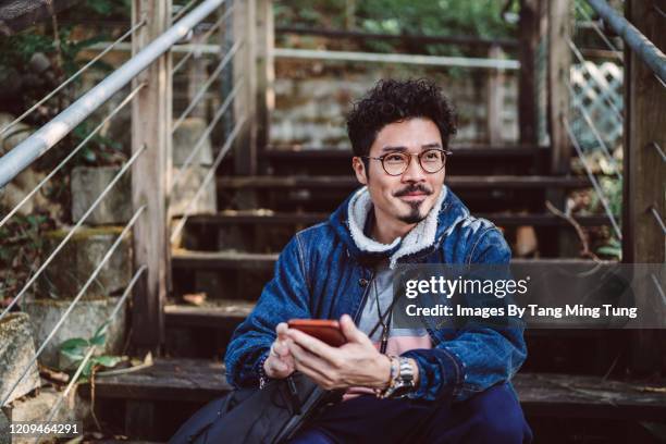 young asian man looking away joyfully while using smartphone in country side - 30-39 years stock pictures, royalty-free photos & images