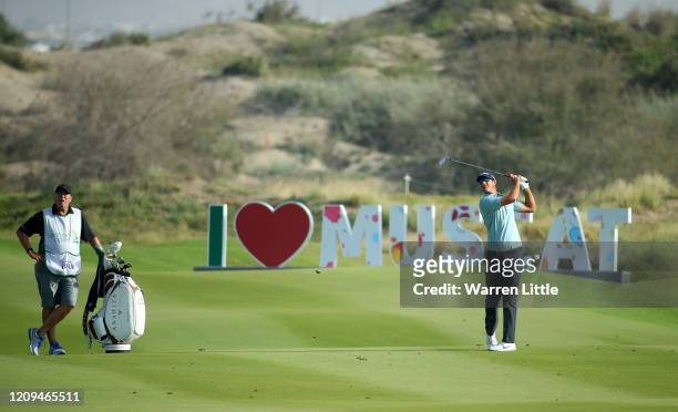 Nicolas Colsaerts of Belgium plays his second shot into the 18th green watched by caddie Brian Nilsson during the third round of the Oman Open at Al...