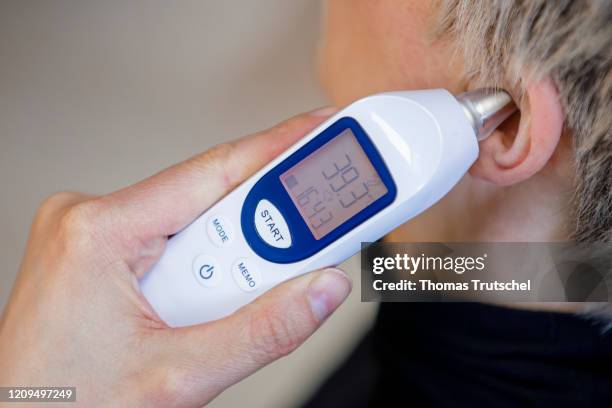 Berlin, Germany Symbol image on the subject of fever. A clinical thermometer is held to an ear and indicates elevated temperature on April 06, 2020...