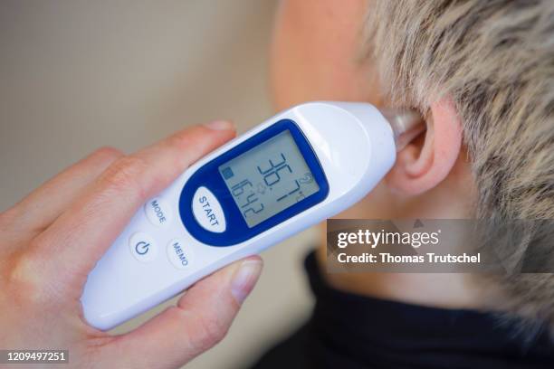 Berlin, Germany Symbol image on the subject of fever. A clinical thermometer is held to an ear and shows normal temperature on April 06, 2020 in...