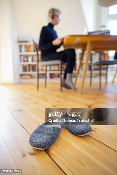 Berlin, Germany Symbol photo on the subject of home office. A woman sits at her desk at home and works on something. Slippers are placed in the...