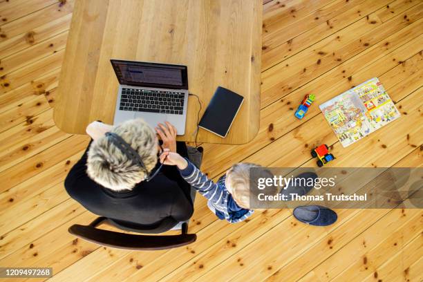 Berlin, Germany Symbol photo on the subject of home office. A woman sits at her desk at home and works. A child is playing next to her on April 06,...