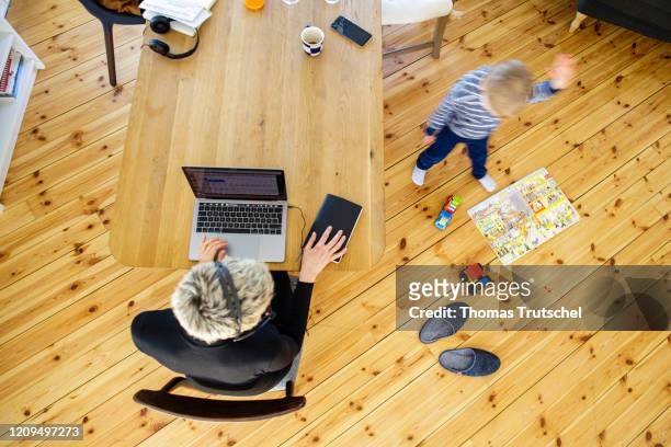 Berlin, Germany Symbol photo on the subject of home office. A woman sits at her desk at home and works. A child is playing next to her on April 06,...