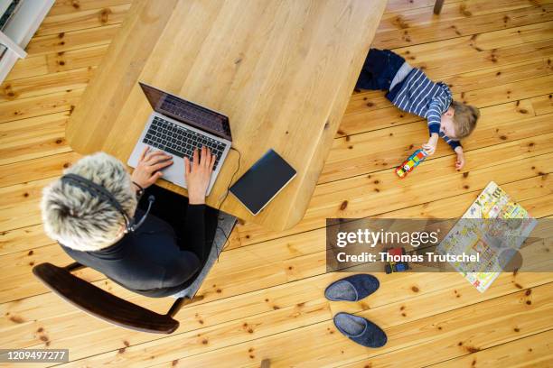 Berlin, Germany Symbol photo on the subject of home office. A woman sits at her desk at home and works. A child is playing next to her on April 06,...