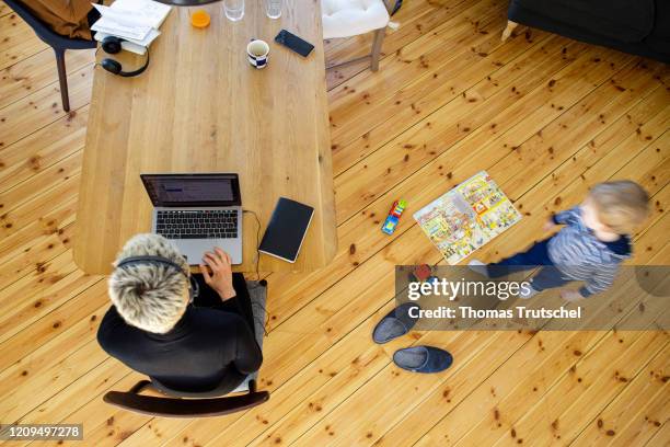 Berlin, Germany Symbol photo on the subject of home office. A woman sits at her desk at home and works. A child is playing next to her on April 06,...