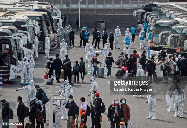 Chinese workers and health officials wear protective white suits as travellers from Wuhan gather to take buses as they are processed and taken to do...