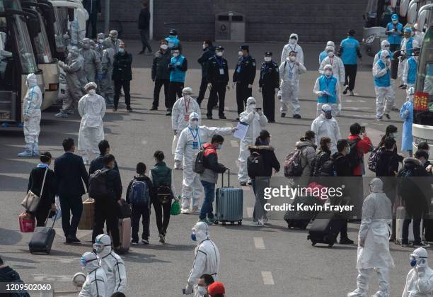 Chinese workers and health officials wear protective white suits as travellers from Wuhan gather to take buses as they are processed and taken to do...