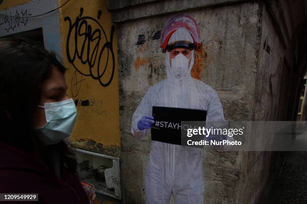 Woman wearing a protective mask walks near a stencil shows a man in a protective suit and a sign that says Stay Home on Cor de Rosa Street, in...