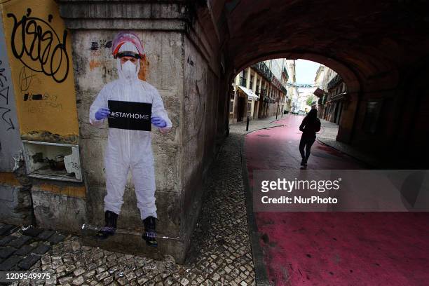 Woman walks near a stencil shows a man in a protective suit and a sign that says Stay Home on Cor de Rosa Street, in Lisbon, on April 8, 2020. Since...
